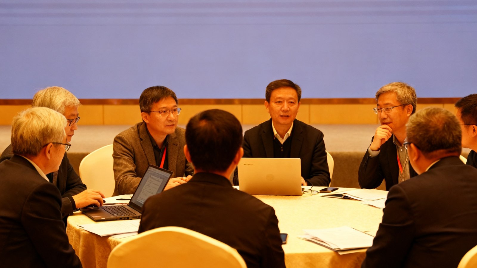 电竞教育与高校课程体系建设研讨会现场，多位学者和行业专家围坐讨论，屏幕上展示着电竞产业人才培养方案